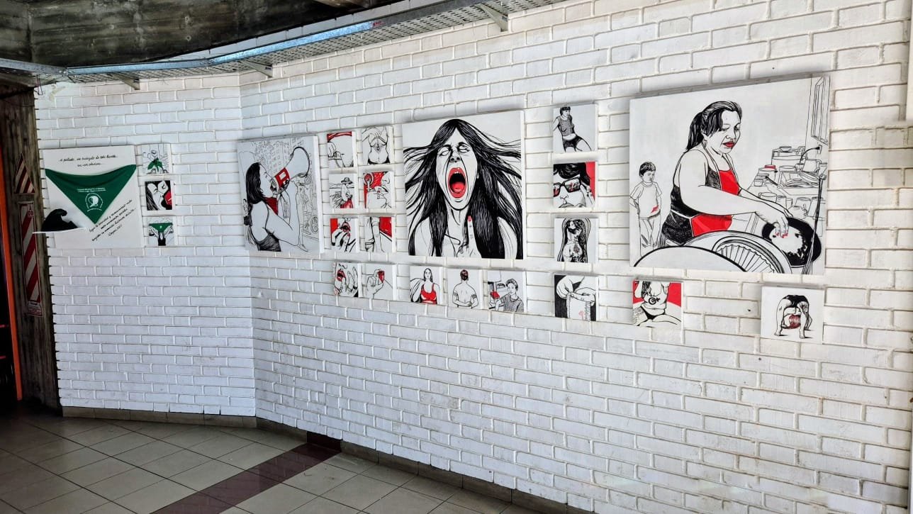 Montaje de obras de mareaoeste en blanco, negro y rojo sobre pared de ladrillo blanco, junto al pañuelo verde, en el II Congreso Regional de Educación Sexual Integral
